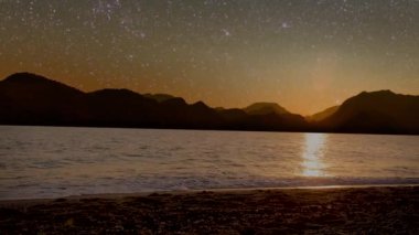 Gece denizi, dağların manzarası ve yıldızlı gökyüzü