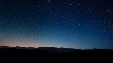 Gece gökyüzünde dağların manzaralı bir yıldız hareketi..