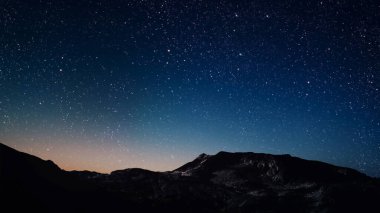 Gece gökyüzünde dağların manzaralı bir yıldız hareketi..