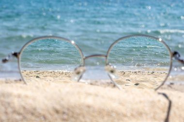 Güneşli bir sahilde, gözlüklerden açık deniz manzarası..