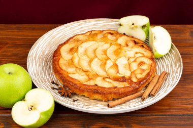 Tarçın çubuklu elmalı turta, anason yıldızı ve kahverengi arka planda ahşap tabakta karanfil. Yan yatay görünüm.