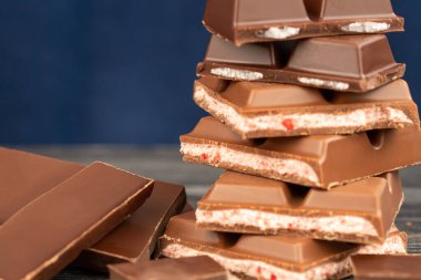 Siyah ahşap masada bir yığın çikolata. Mavi arkaplan.