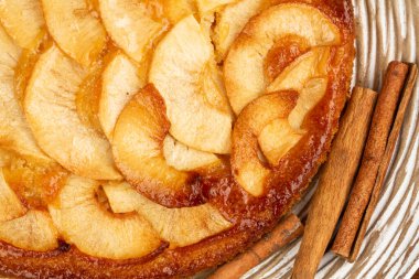 Apple pie with cinnamon sticks on wooden plate.