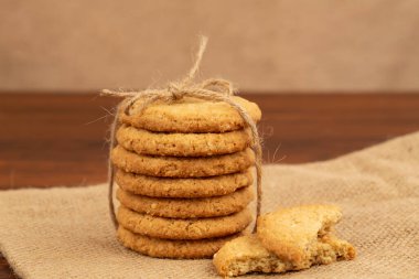 Tahta sehpadaki çuval bezinde iple bağlanmış susam tohumlu yulaf ezmeli kurabiyeler. Bej arka plan. Ön görünüm.