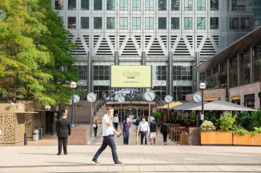 Londra, Birleşik Krallık - 6 Eylül 2021 - Canary Wharf finans bölgesi şirket binaları ve saatleriyle. Reklam panosu ortadaydı. İş alanında yürüyen insanlar.