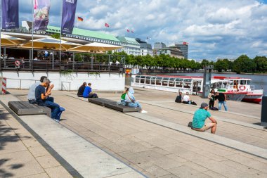 Hamburg, Almanya - 14 Temmuz 2024 - Hamburg, Alster 'daki merdivenlerde oturan insanlar. Güneşli bir yaz günü insanlar Hamburg 'un merkezinde dinleniyor. Alster 'da turistik tekneler.