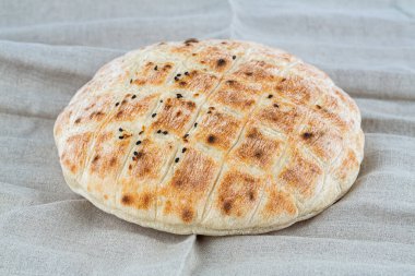 Gri kumaş arka planında susam tohumlu yuvarlak ekmek. Gri kumaş havlunun üzerinde taze pişmiş ekmek..