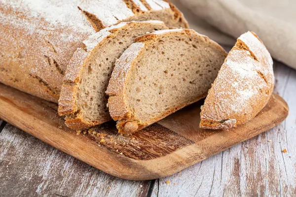 Tahta üzerinde bej kumaşlı taze pişmiş köy ekmeği. Tahtada uzun taze ekmek.