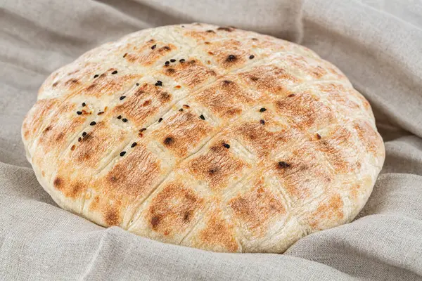 Gri kumaş arka planında susam tohumlu yuvarlak ekmek. Gri kumaş havlunun üzerinde taze pişmiş ekmek..
