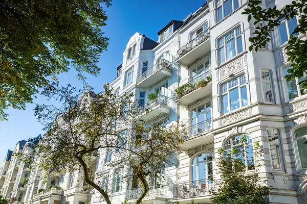 Duvarlarında muhteşem süslemeler olan beyaz konut binası. Binada yeşil ağaçlar var.