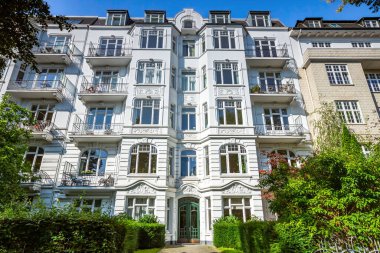 Duvarlarında muhteşem süslemeler olan beyaz bina girişi. Binadaki ağaçlar ve çalılar.