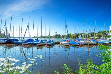 Almanya 'nın Hamburg şehrinde güneşli bir yaz gününde Alster Nehri' nde yelkenli gemiler. Kayıklar su yüzeyinde yaprakları yansıtıyor..