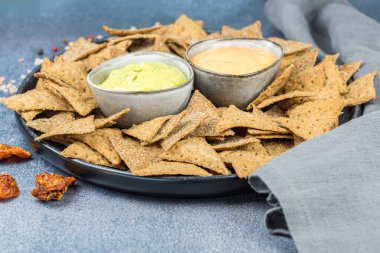 Siyah seramik tabakta krakerler, otlar ve peynir sosları, kurutulmuş domatesler, renkli biberler ve gri arka planda tuz..