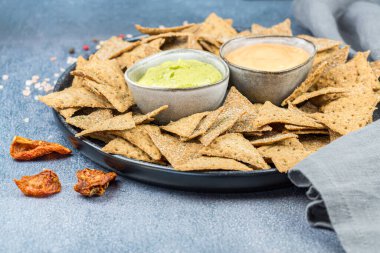 Siyah seramik tabakta krakerler, otlar ve peynir sosları, kurutulmuş domatesler, renkli biberler ve gri arka planda tuz..