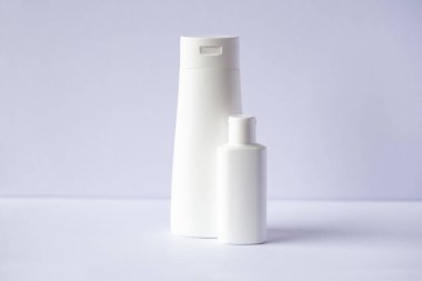 Gri arka planda iki beyaz cilt bakım ürünü var. Gri üzerine bir şişe kozmetik..