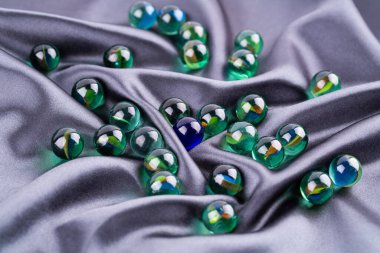 Gri kumaş arka planda renkli cam toplar. Yuvarlak yeşil dekoratif taşlar..