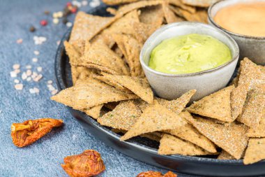 Siyah seramik tabakta krakerler, otlar ve peynir sosları, kurutulmuş domatesler, renkli biberler ve gri arka planda tuz..