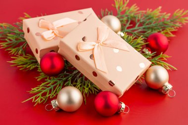 Kırmızı arka planda kurdeleli bej hediye kutuları. Hediye kutuları, Noel baloları ve kırmızı üzerine köknar ağacı dalları..