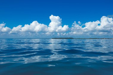 Bulutlar mavi gökyüzünde sakin denizin üzerinde güneş ışığı yansımasıyla