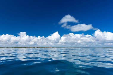 Bulutlar mavi gökyüzünde sakin denizin üzerinde güneş ışığı yansımasıyla