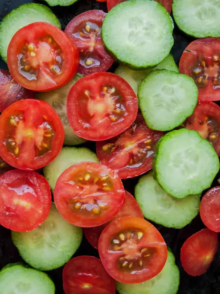 Mevsimlik diyet ve beslenme, sağlıklı yeme konsepti. Dilimlenmiş taze kırmızı kiraz domatesleri ve siyah arka planda salatalıklar, su damlalarıyla kaplı sebzelerin üst görüntüsü..