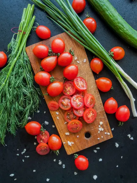 Mevsimlik diyet ve beslenme, sağlıklı yeme konsepti. Bitkilerle kaplı taze kırmızı kiraz domatesleri ve masanın üzerindeki tahtaya deniz tuzu serpiştirilmiş pırasa..