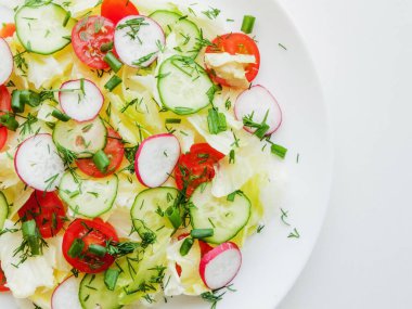 Ev yemeği ve sağlıklı beslenme konsepti. Taze bahar salatası dilimlenmiş turp, kiraz domatesleri, salatalık, yeşillik ve zeytinyağına bulanmış buzdağı salatası, vitamin yemeğiyle kaplı tabağın üst görüntüsü..