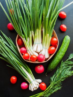 Mevsimlik diyet ve beslenme, sağlıklı yeme konsepti. Taze kırmızı kiraz domatesleri, yeşil pırasa, turp ve salatalık sepeti arka planda, sebzelerin üst görüntüsü..