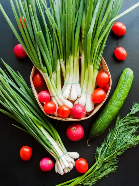 Mevsimlik diyet ve beslenme, sağlıklı yeme konsepti. Taze kırmızı kiraz domatesleri, yeşil pırasa, turp ve salatalık sepeti arka planda, sebzelerin üst görüntüsü..