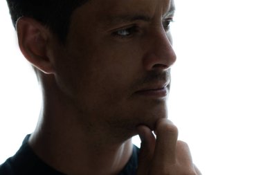 Eli çenesinde, beyaz bir arkaplanda düşünen bir adamın karanlık yakın plan portresi.