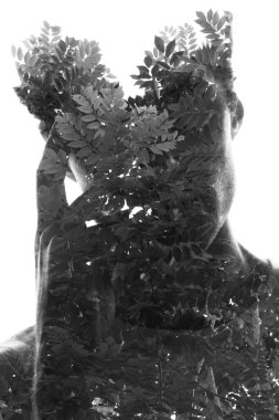 Siyah ve beyaz, yüzünü bir elle tutan bir adamın portresi ağaç dalları siluetiyle sanatsal bir şekilde birleştirilmiş..