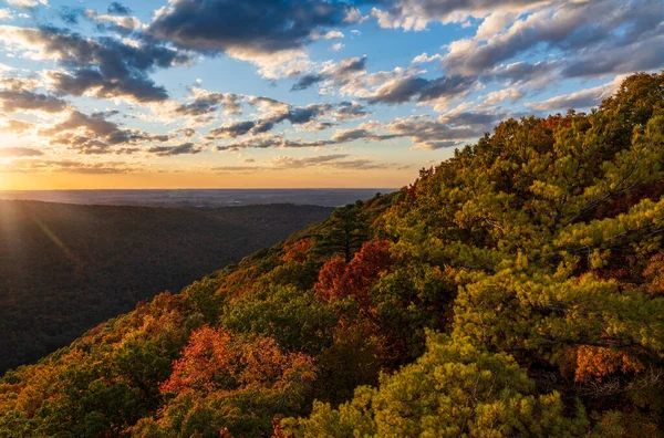 クーパー ロック州立の森の木々の秋の色を照らす雲の後ろに沈む太陽 — ストック写真