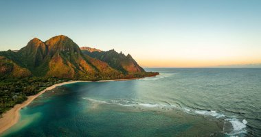 Sabahın ilk ışıklarının geniş panoramik görüntüsü. Dağları yakalıyor. Kauai 'de, Na Pali dağlarıyla birlikte tünellerin kumsalına hükmediyor.