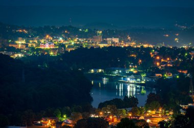 Batı Virginia 'daki Morgantown şehrinin gece manzarası. Nehirde ışıklar ve yansımalar var. Üniversite kampüsü uzakta.
