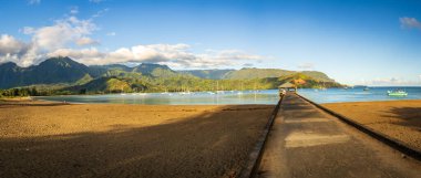 Panorama of the famous pier and sandy beach of Hanalei Bay just after sunrise with the sands still empty of people clipart