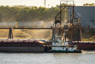 Römorkör, yük mavnalarını tahıl yükleme limanından geçiriyor. Doğu St. Louis Illinois 'de güneş ışığı alan toz dolu.