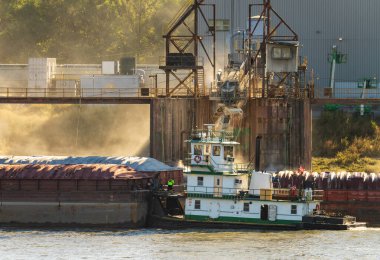 Römorkör, yük mavnalarını tahıl yükleme limanından geçiriyor. Doğu St. Louis Illinois 'de güneş ışığı alan toz dolu.