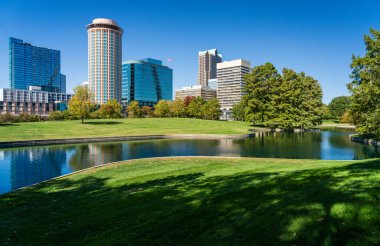 Gateway Arch Parkı 'nın yeşil ekimini ve gölün karşısındaki St. Louis Missouri şehir merkezindeki ofis binalarına ve otellere bakın.