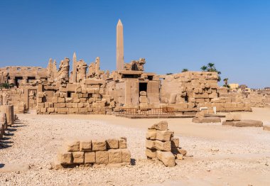 Hiyerogliflerle kaplı antik Mısır dikilitaşları, Karnak tapınağının kalıntılarıyla çevrili açık mavi gökyüzüne karşı dimdik ayakta duruyor.