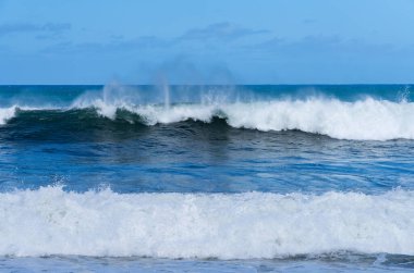 Mavi gökyüzünün altında kıyıya vuran okyanus dalgaları, Lumahai sahilinde dalgalanan ve sıçrayan turkuaz su.