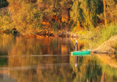 Geleneksel galakside Nil nehrinin kıyısında küçük yeşil bir kayıkta balık tutan bir adam.