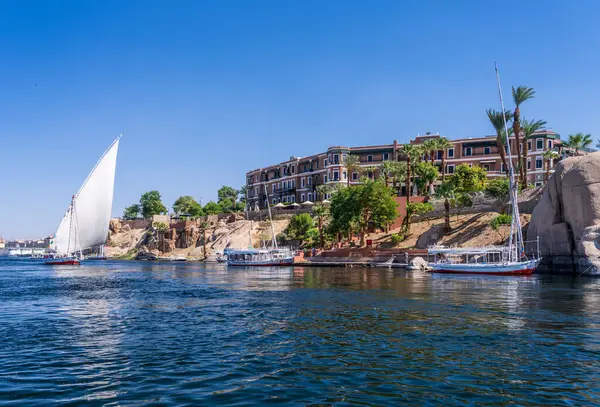 Aswan, Mısır - 4 Kasım 2024: Felucca eski Cataract Oteli 'nin yanındaki Nil' de bir gemi gezisine yelken açıyor.