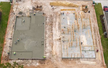 İşçiler beton döşemeyi pürüzsüz ve cilalarken, diğer inşaat işleri yeni ev için çivi iskeleti