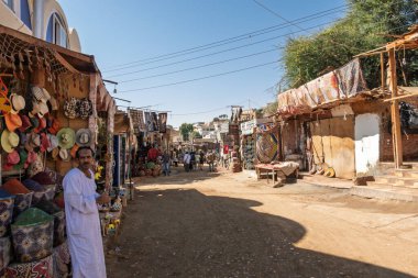 Aswan, Mısır - 5 Kasım 2024: Uzakta turistlerin bulunduğu Nubian Village 'da geleneksel sokak pazarı