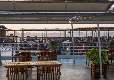 Güneş, Edfu Mısır 'daki başka bir gemiye kenetlenmiş Nil yolcu gemisinin güvertesindeki masa ve sandalyelerin üzerinden yükseliyor.