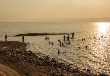 Günbatımında modern bir otelin sahilindeki Ölü Deniz sularında turistler