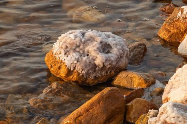 Yakından bakınca, ölü denizin kenarındaki kayaların üzerinde bulunan eşsiz tuz oluşumlarının güneş ışığında parladığını görüyoruz.