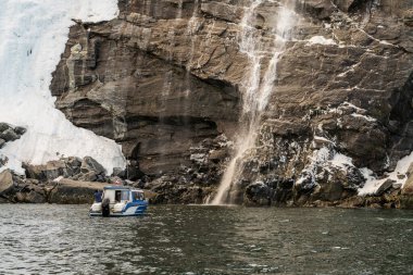 Iceberg tour power boat on fjord by waterfall running off Saddle Mountain near the capital city of Nuuk in Greenland