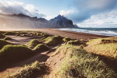 Güneş ışığıyla parlayan alışılmadık tepeler. Dramatik ve muhteşem bir sahne. Turist eğlencesi. Stoksnes Burnu, Vestrahorn (Mt. Batman), İzlanda, Avrupa. Bağbozumu etkisi. Instagram filtresi. Güzellik dünyası.