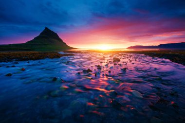 Akşam Kirkjufell volkanı Snaefellsnes yarımadasının kıyısında. Kirkjulsfoss 'un yeri. Tipik İzlanda manzarası. İklim değişikliği. Duvar kağıdının harika bir görüntüsü. Dünyanın güzelliğini keşfedin.